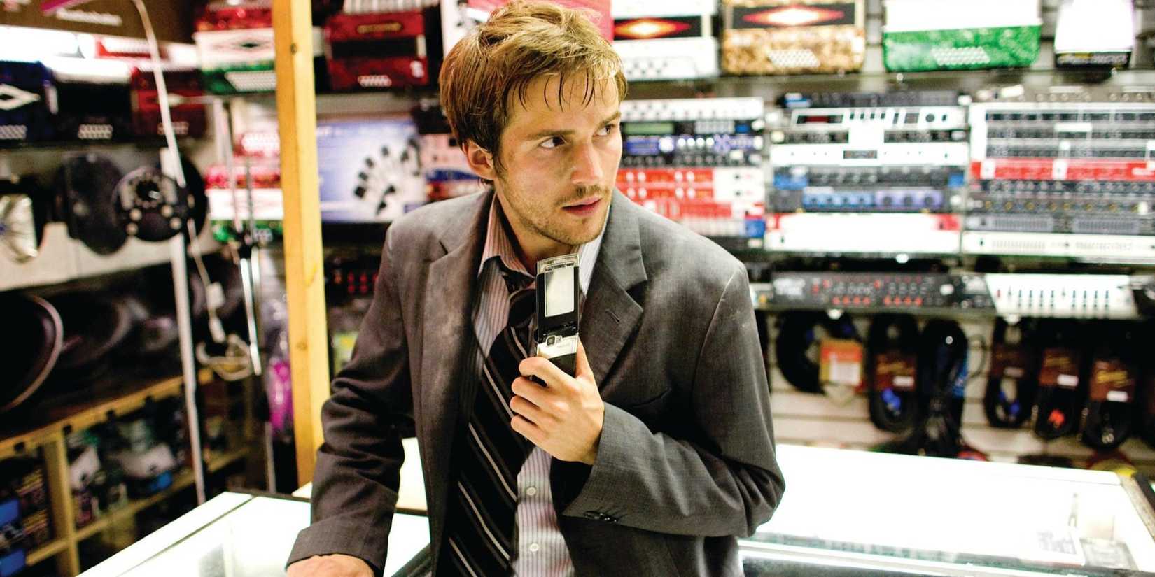 Rob Hawkins in Cloverfield 2008 holding a phone in a tech shop