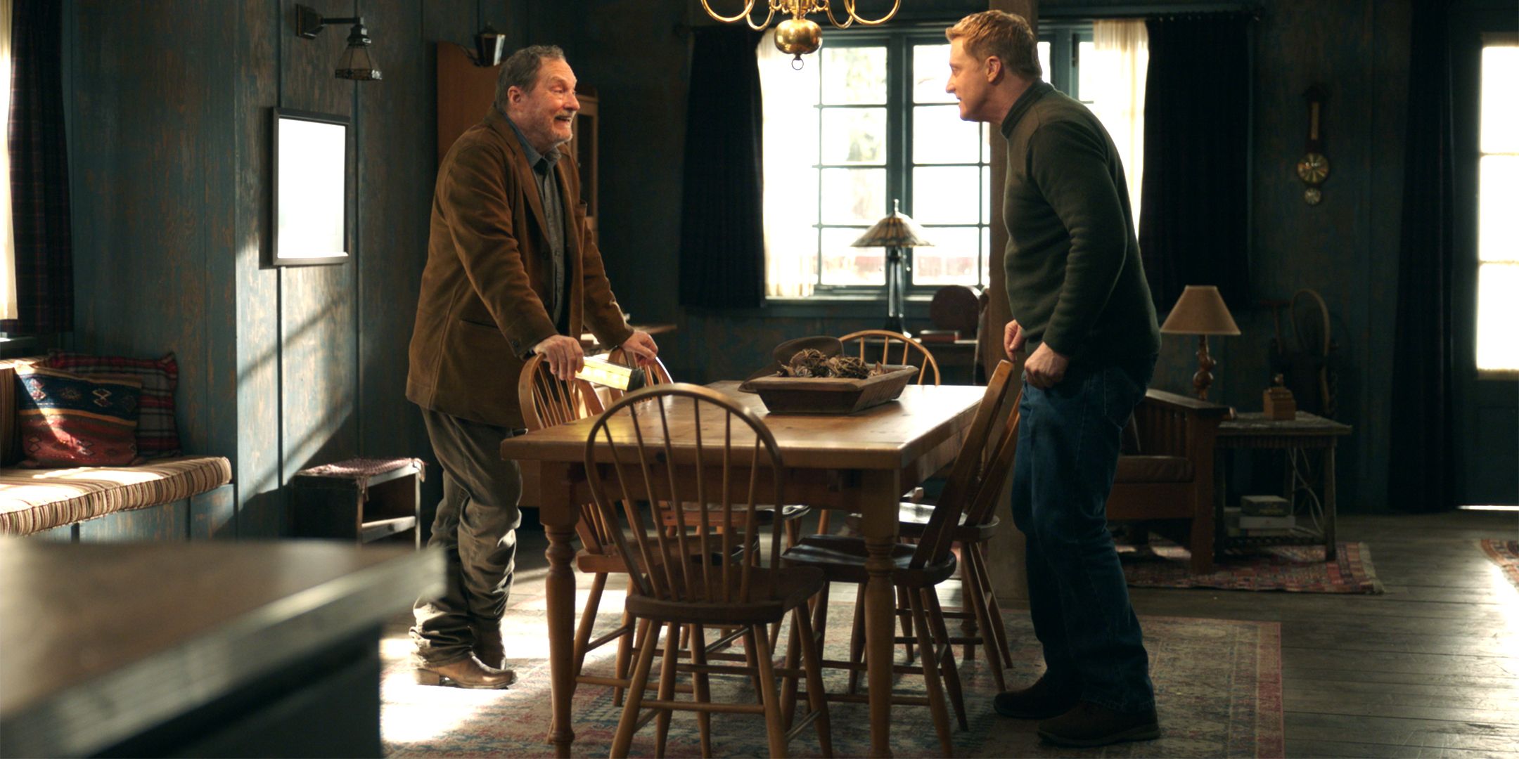 Stephen Root's Ed smiling and Alan Tudyk's Harry looking awkwardly while standing at dining table in Resident Alien season 4