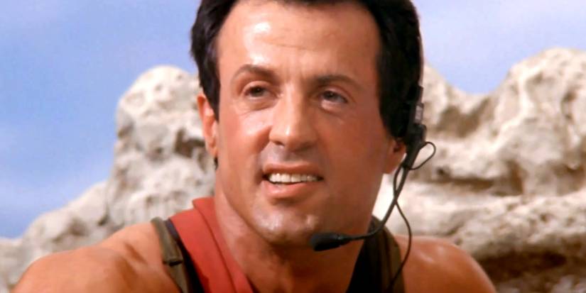 Sylvester Stallone is smiling while helping someone in Cliffhanger
