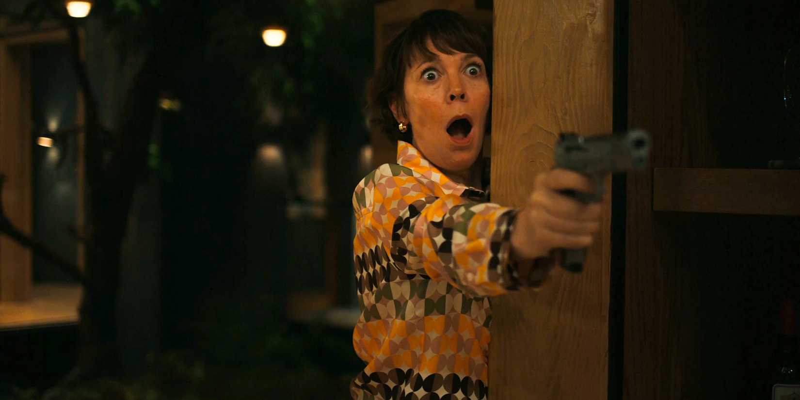Olivia Colman segurando uma arma e com uma expressão chocada em The Roses