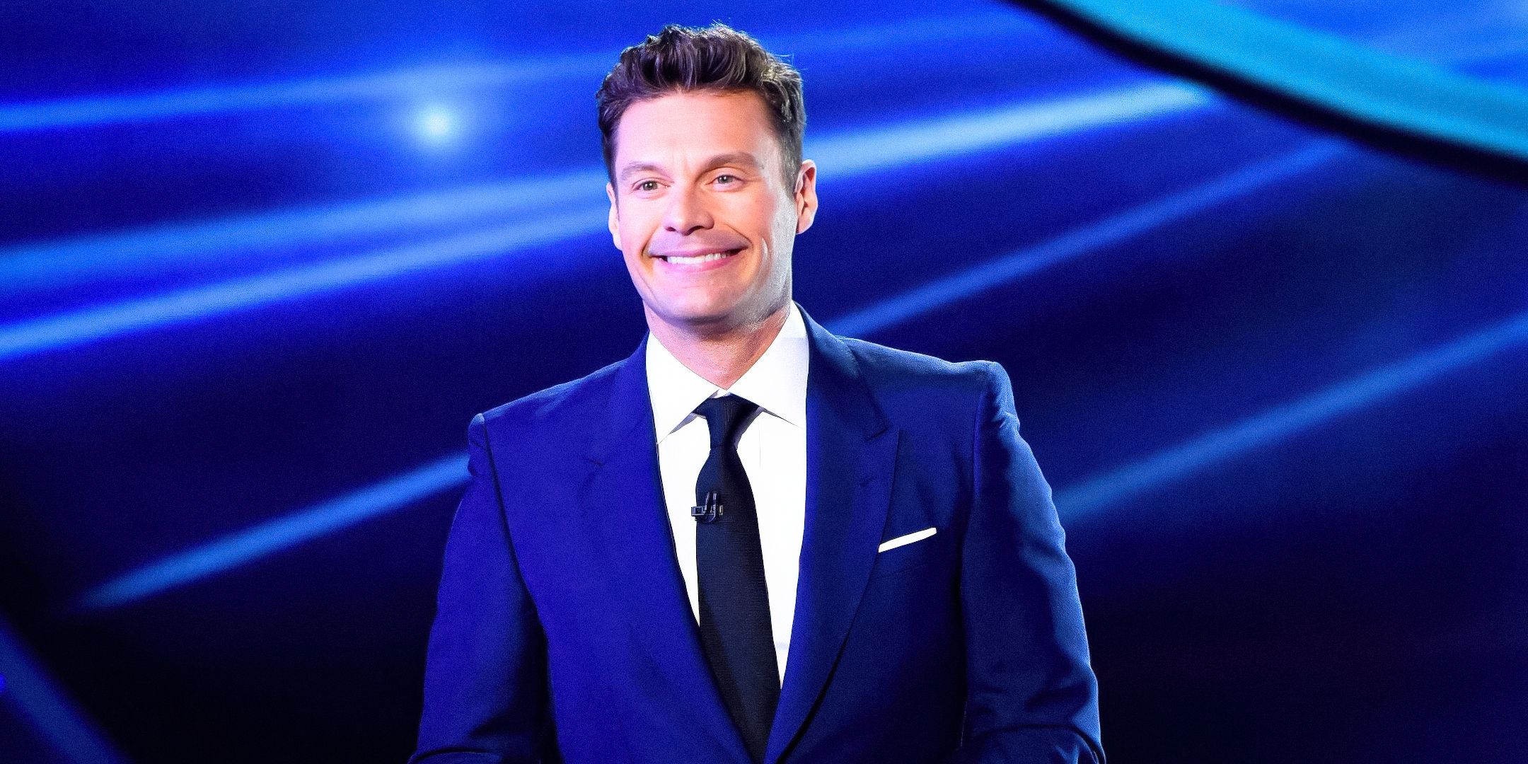 Ryan Seacrest sorridente davanti a uno sfondo blu