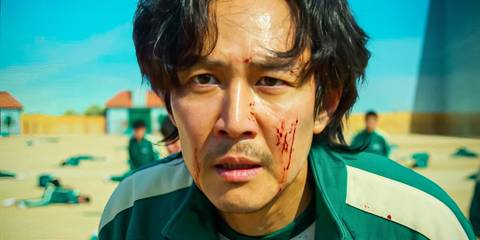Gi-hun with blood on his face while dead body lie in the background in Squid Game season 1