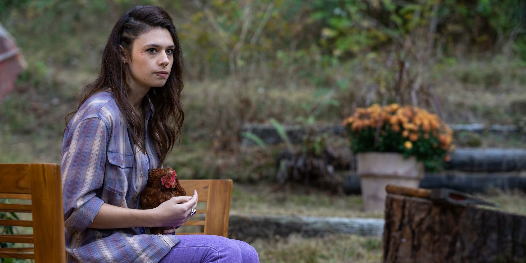 Lisa sitting on a bench, holding a chicken, and looking up at Natalie in Yellowjackets season 2, episode 3