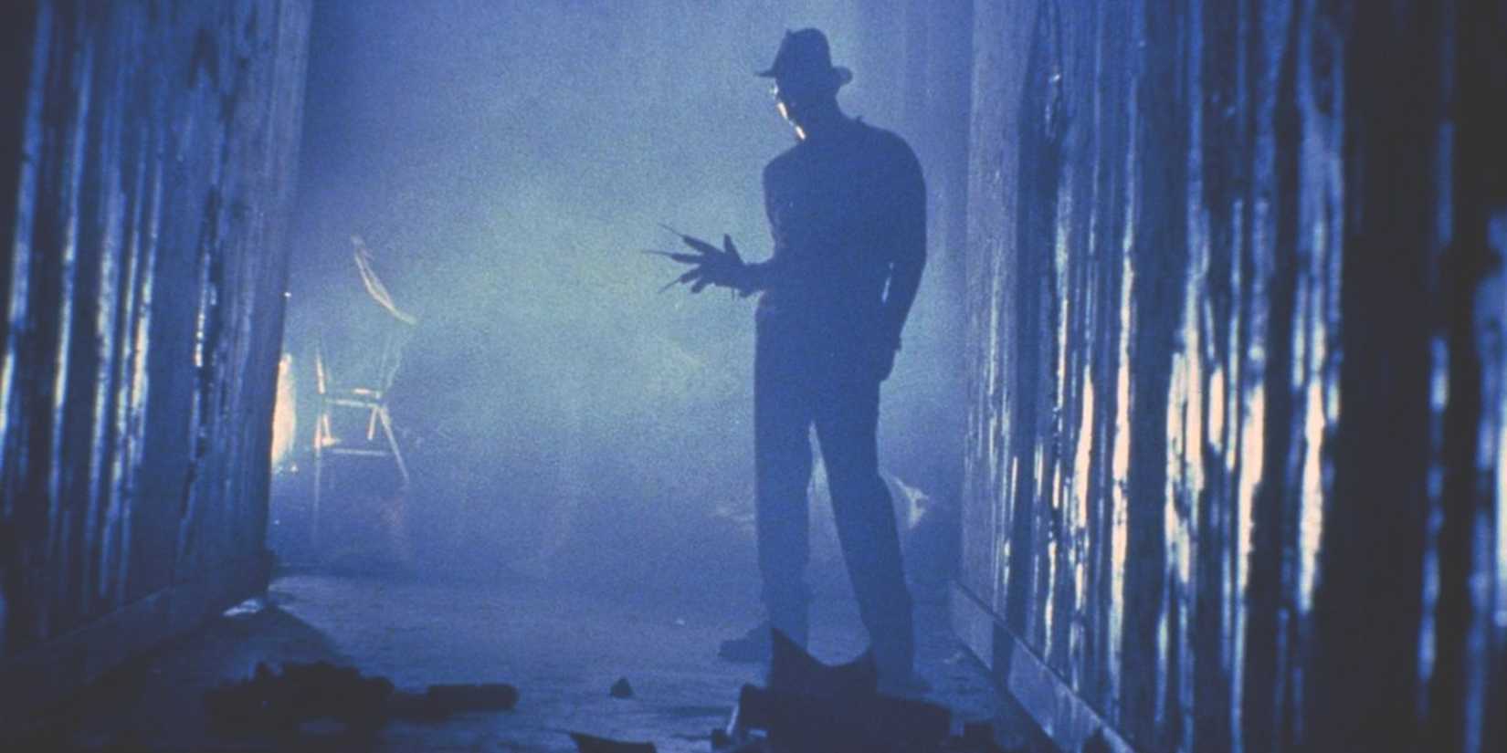 Freddy Krueger holds out his claw hand while standing in a shadowy hallway in A Nightmare on Elm Street
