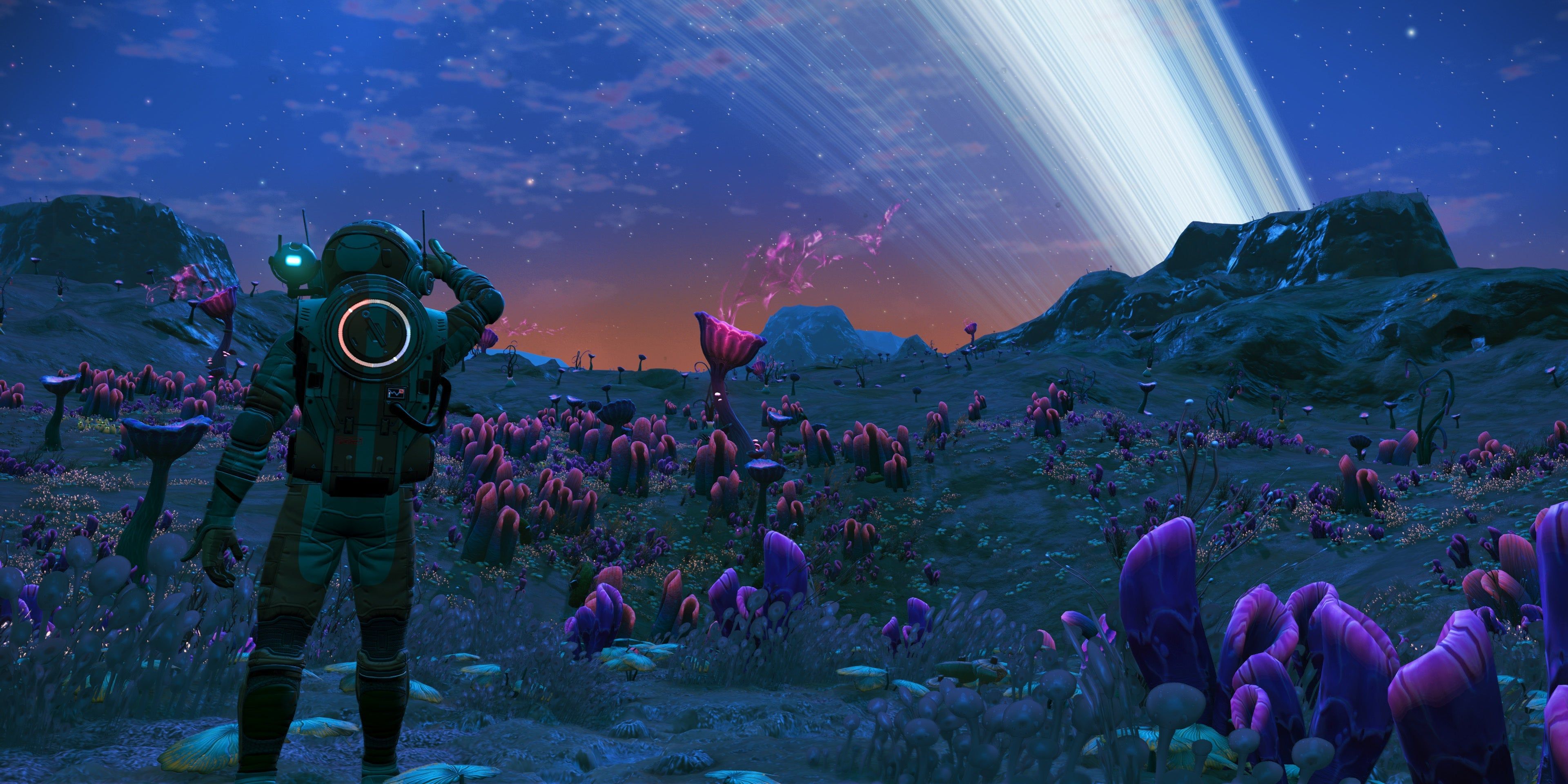 A player character in No Man's Sky looking at the planet's rings over a rocky ridge at sunset.