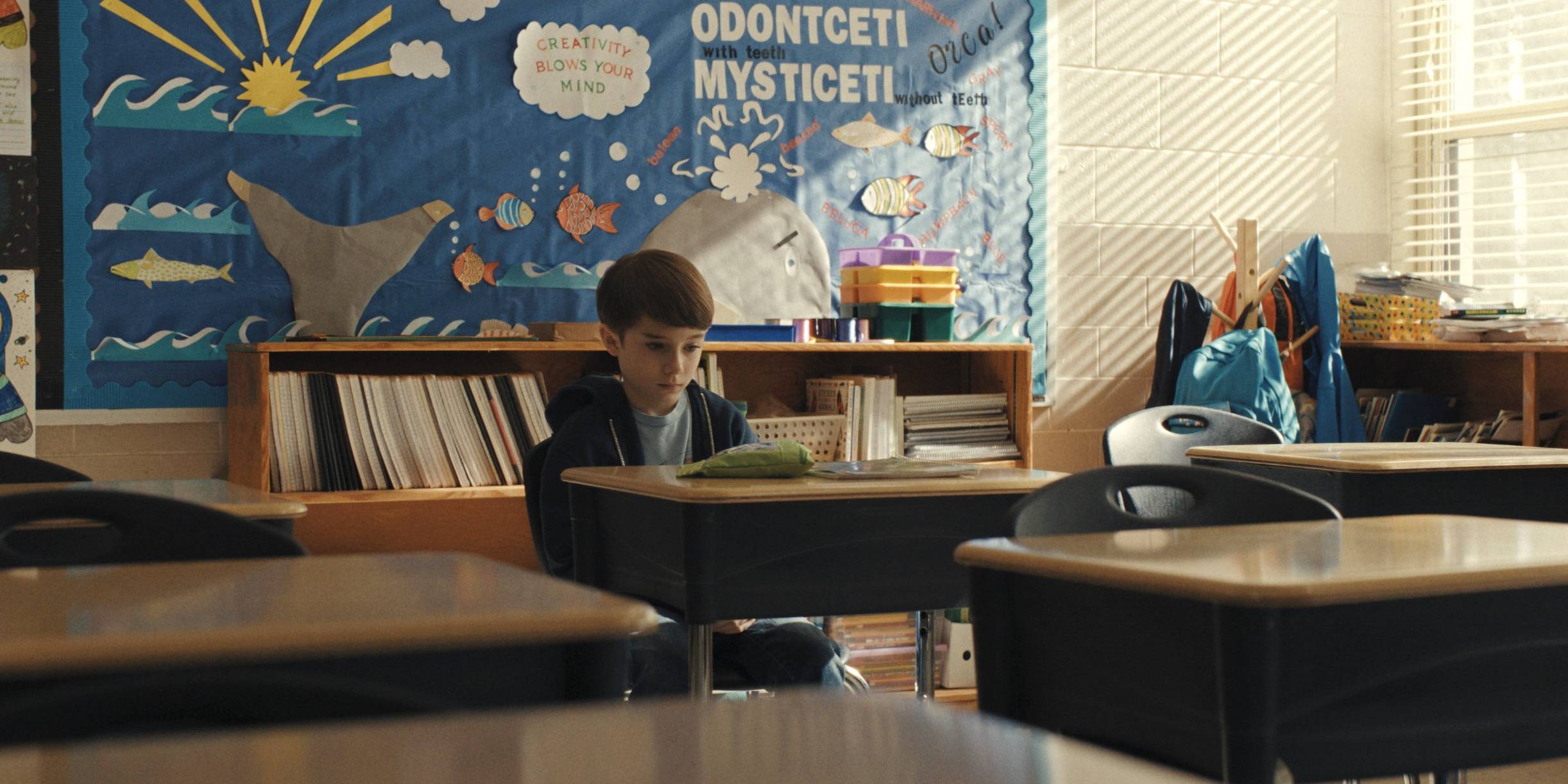 Alex sitting at his desk alone in the classroom in Weapons