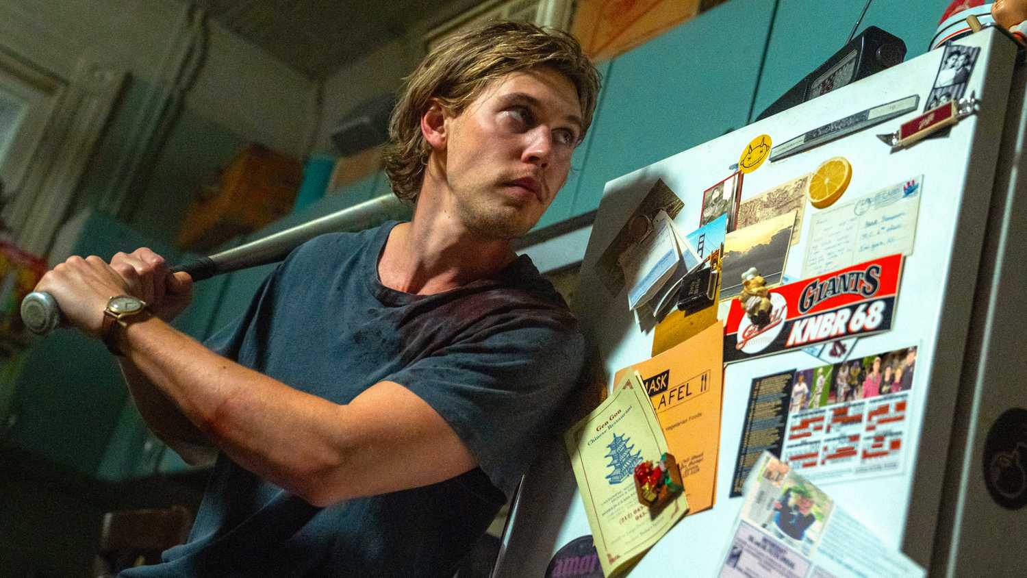 Austin Butler memegang tongkat baseball sambil berdiri di samping lemari es di Caught Stealing