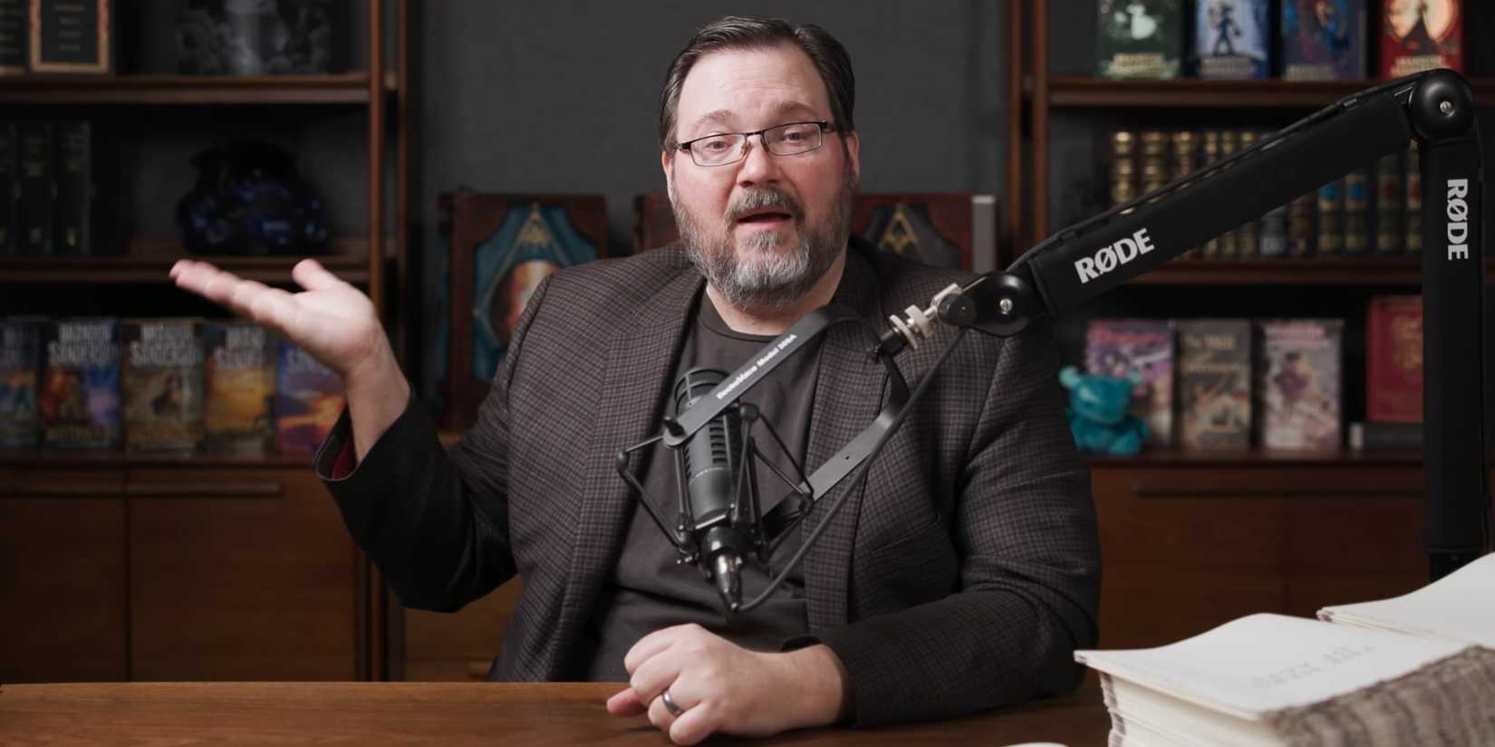 Brandon Sanderson lifts his hand to the side.