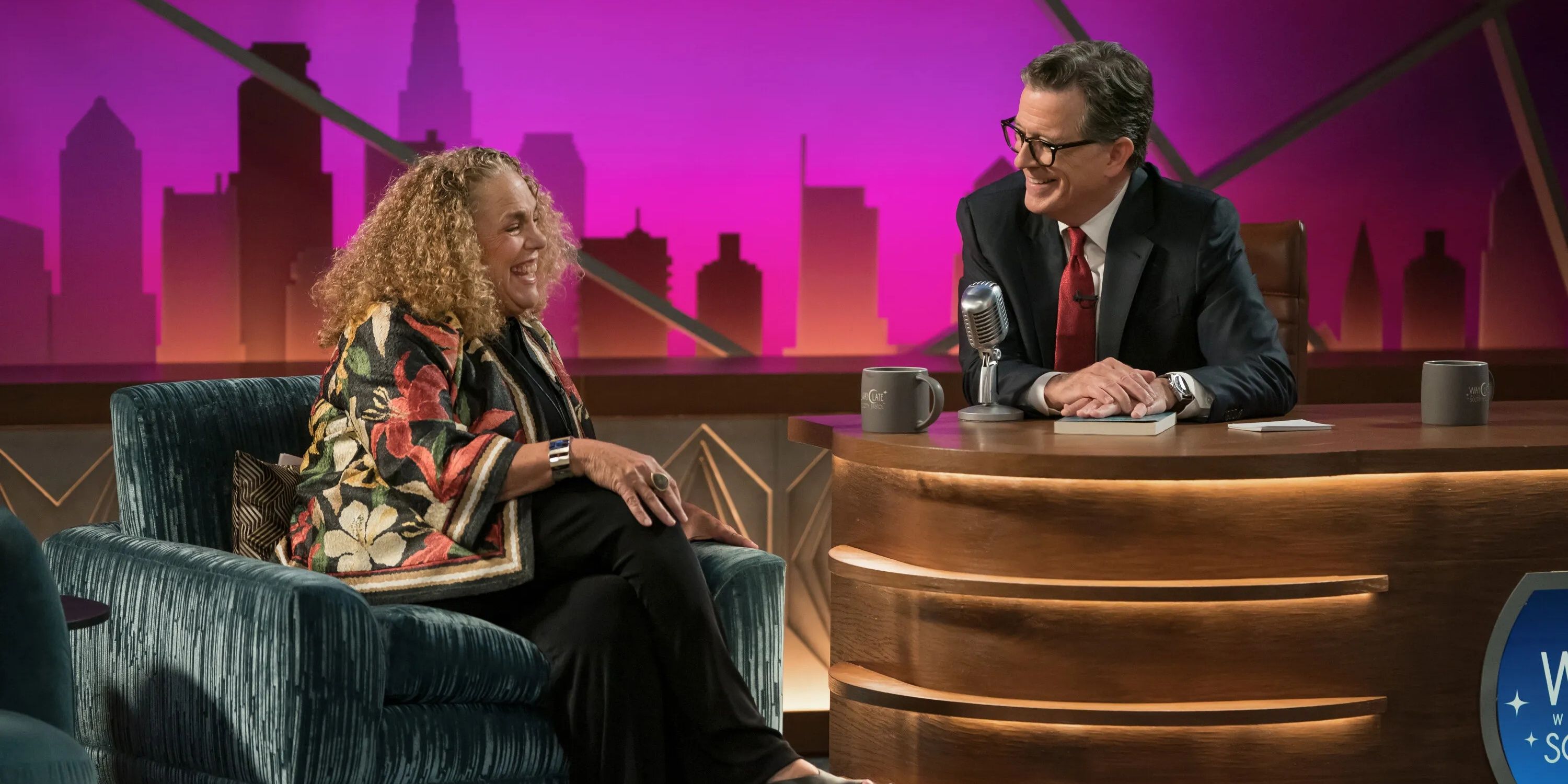 Marcia DeBonis as Sheryl Jacobs and Stephen Colbert as Scotty Bristol on a late-night show in Elsbeth season 3