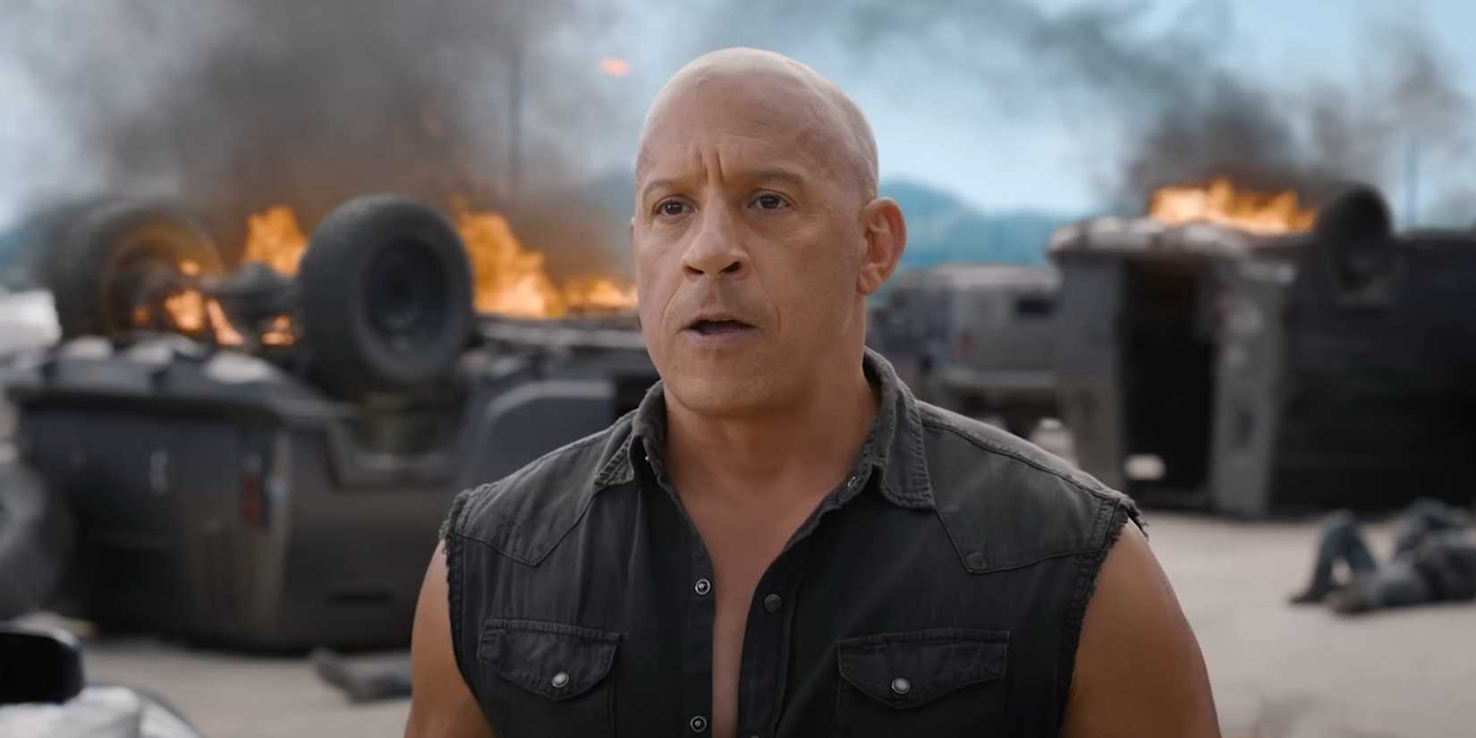 Vin Diesel as Dominic Toretto stands in front of burning trucks in Fast X