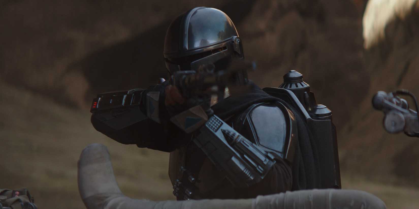 Din Djarin (Pedro Pascal) aims his pulse rifle over the seat of his speeder bike on Tatooine.