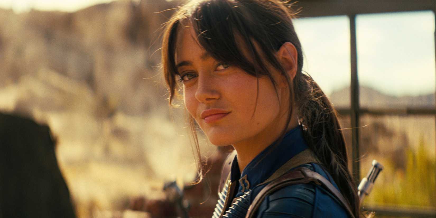 Ella Purnell as Lucy MacLean wearing her vault suit and smirking softly in Fallout season 2