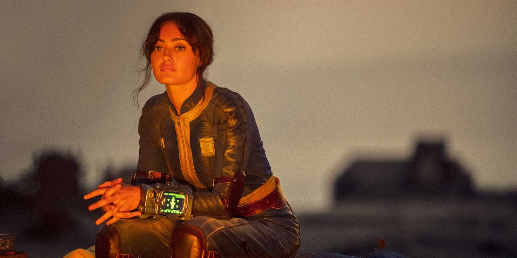 Ella Purnell's Lucy looking thoughtfully while sitting next to a fire in Fallout season 1