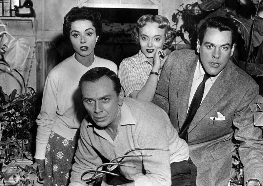 The cast of Invasion of the Body Snatchers look at something in horror while standing in a greenhouse