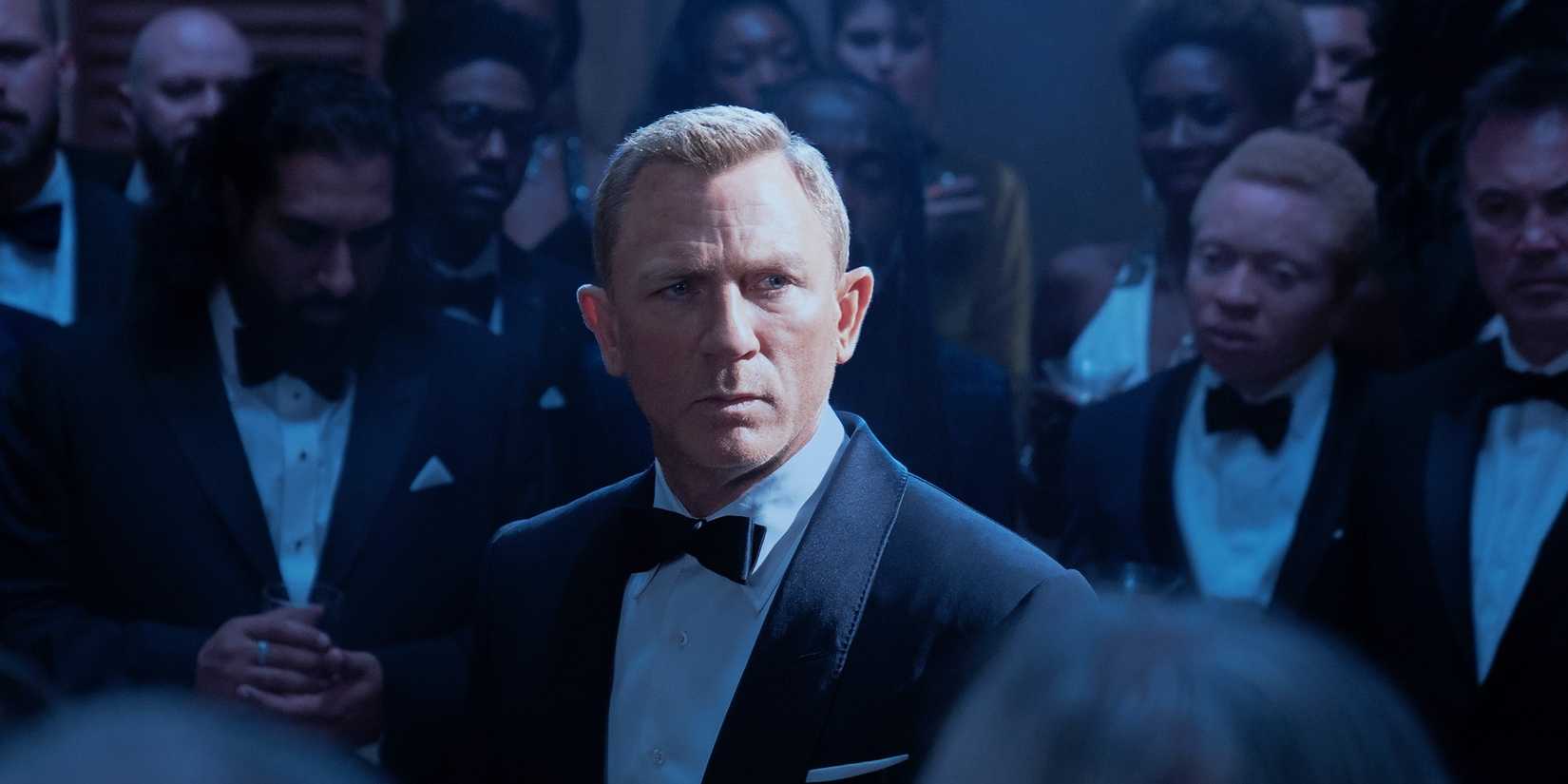 James Bond surrounded by a bunch of people in tuxedos in No Time to Die