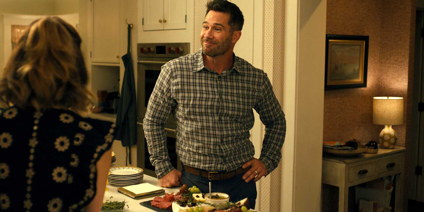 Luke Macfarlane's Charlie looking surprised and smiling while standing in kitchen in Platonic season 2