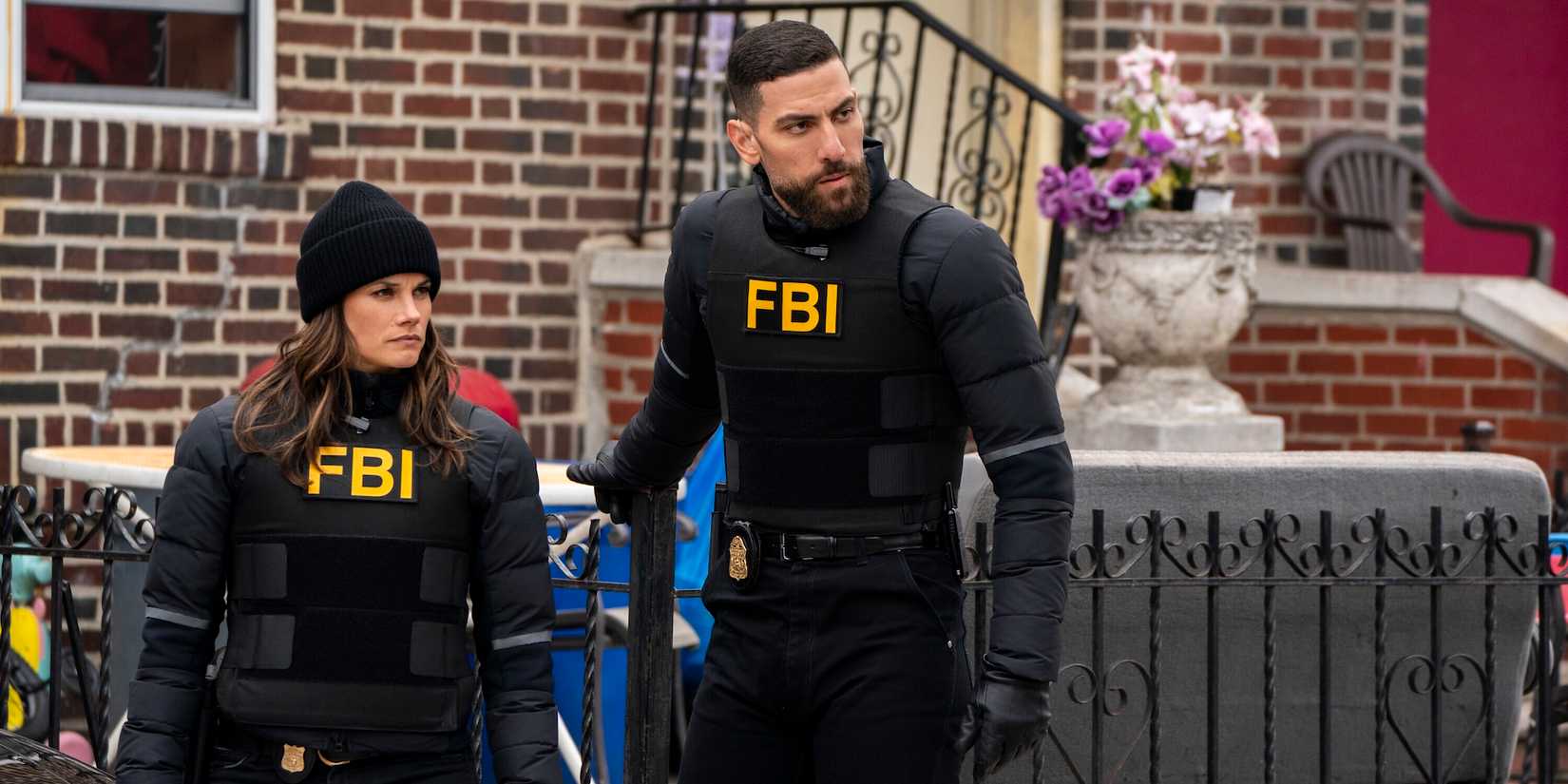 Maggie and OA don bullet-proof vests while standing outside of a brick home on FBI