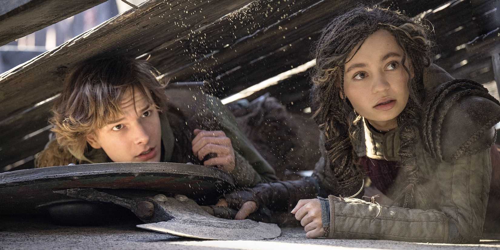Mason Thames as Hiccup and Nico Parker as Astrid under a wooden board in How To Train Your Dragon