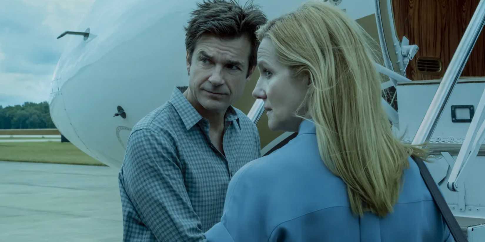 Marty (Jason Bateman) and Wendy (Laura Linney) looking over their shoulders while standing next to a plane on a runway in Ozark.