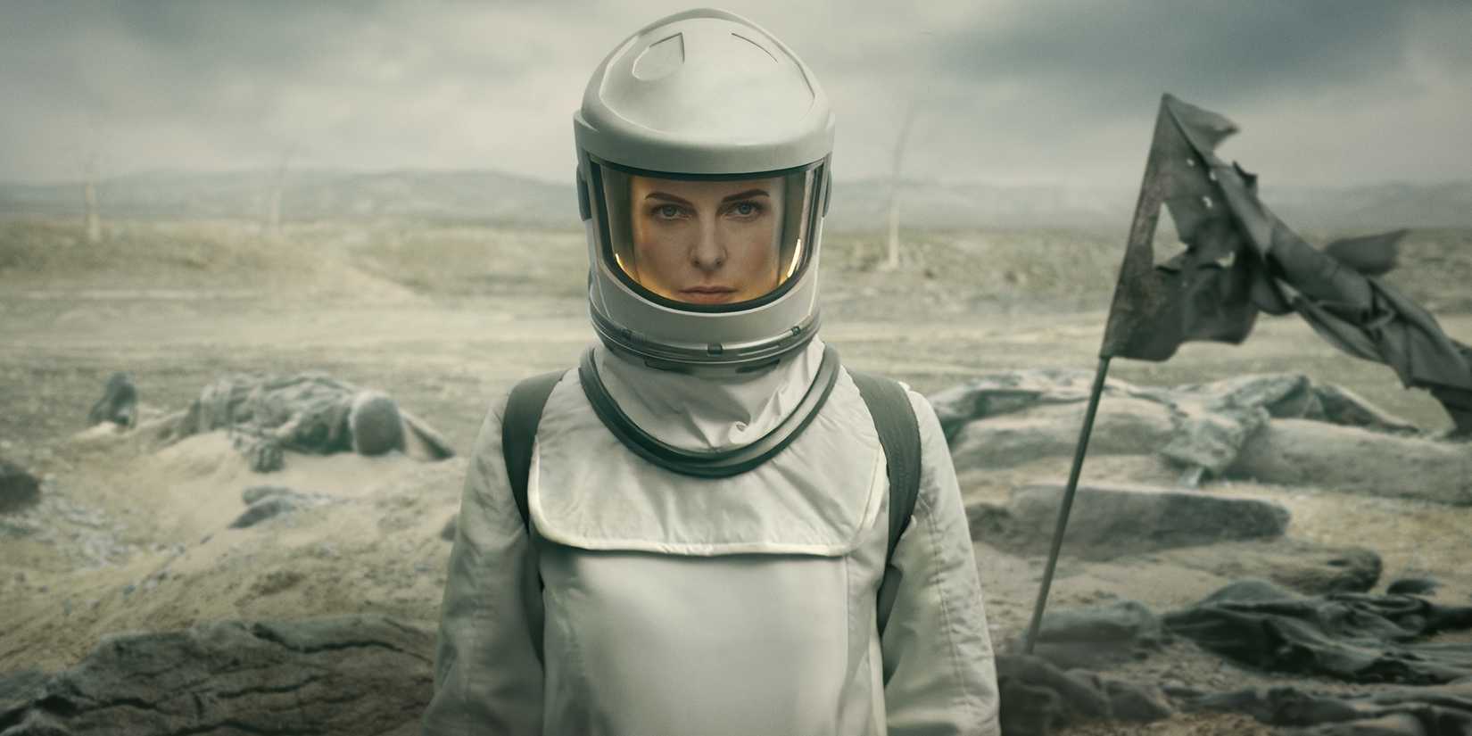 Rebecca Ferguson as Juliette wearing her suit and walking outside in front of corpses and a tattered flag in Apple TV+'s Silo