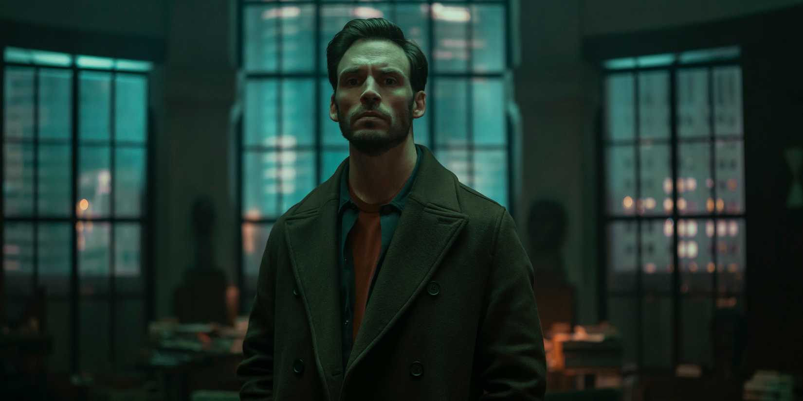 Sam Claflin stands in an office in Lazarus
