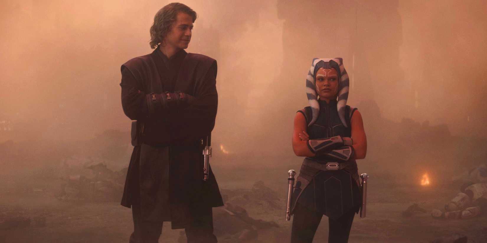 Anakin Skywalker (Hayden Christensen) stands beside Ahsoka Tano (Ariana Greenblatt) and looks down at her, with both their arms crossed.