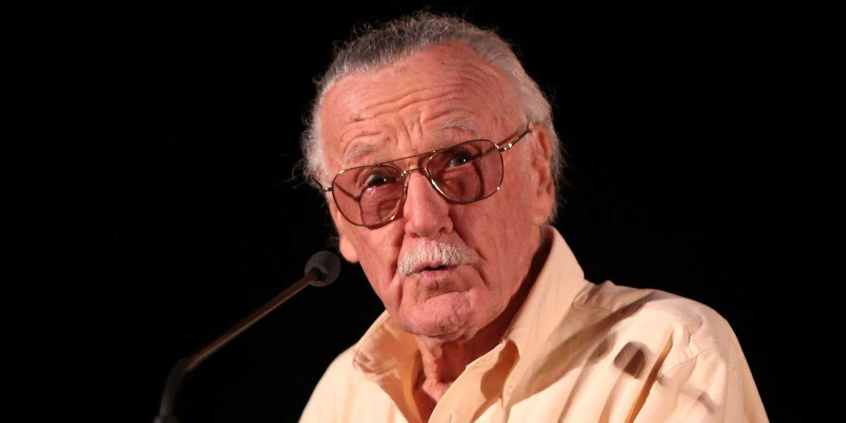 Stan Lee at a podium against a black backdrop