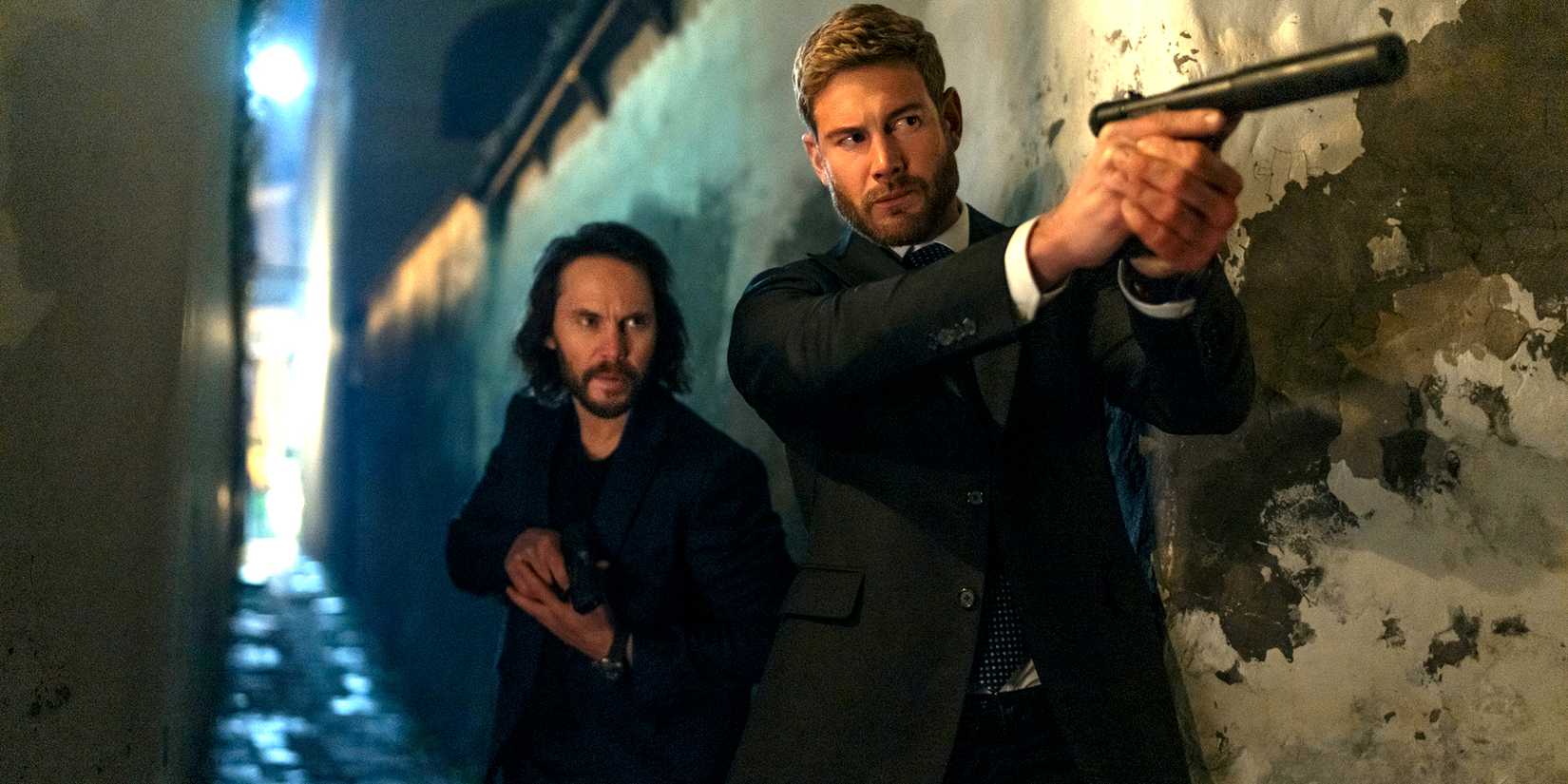 Taylor Kitsch's Ben squatting behind Tom Hopper's Raife while they both hold guns in The Terminal List: Dark Wolf
