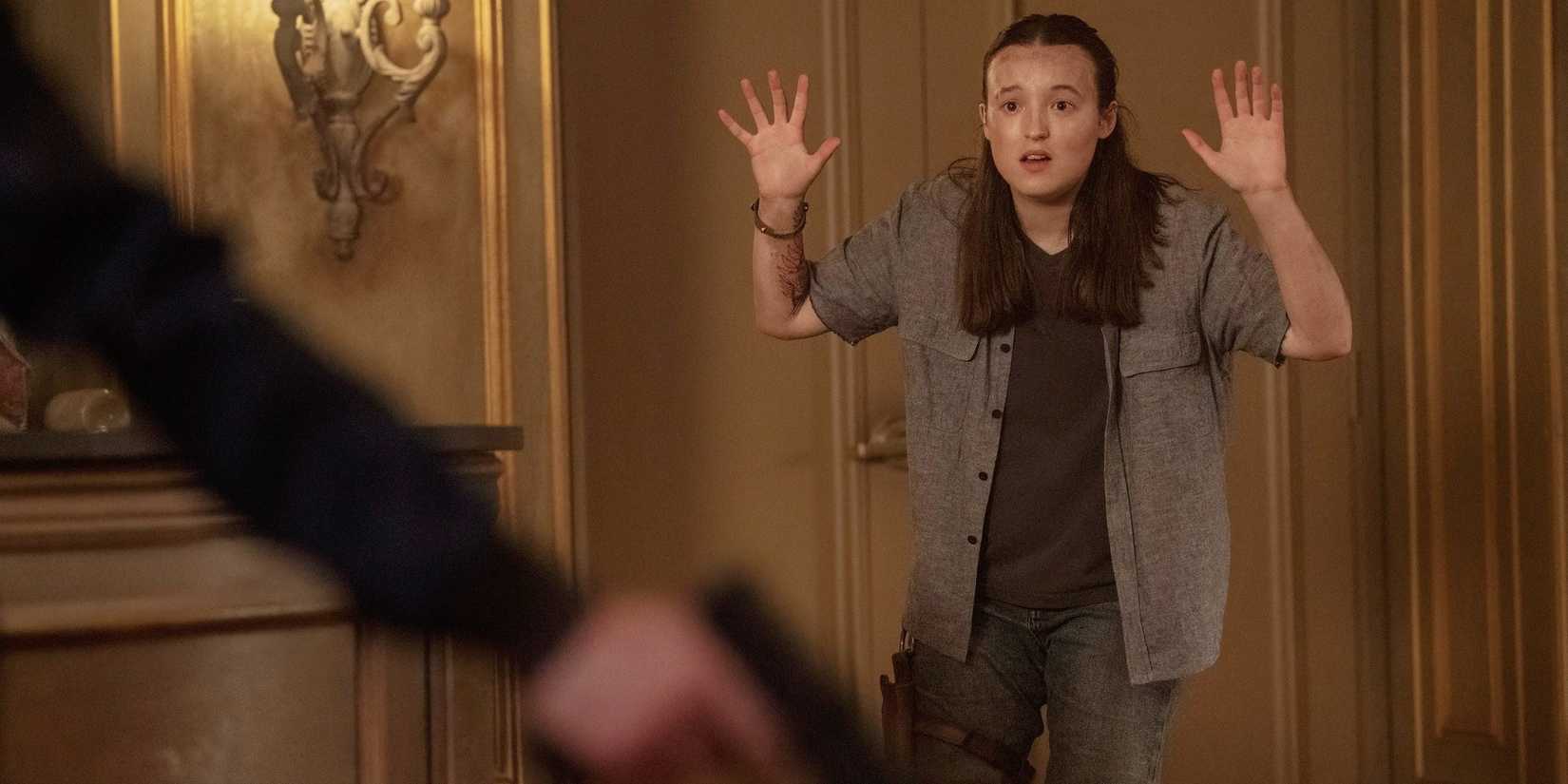 Ellie raising her hands while a gun is brandished at her in The Last of Us season 2