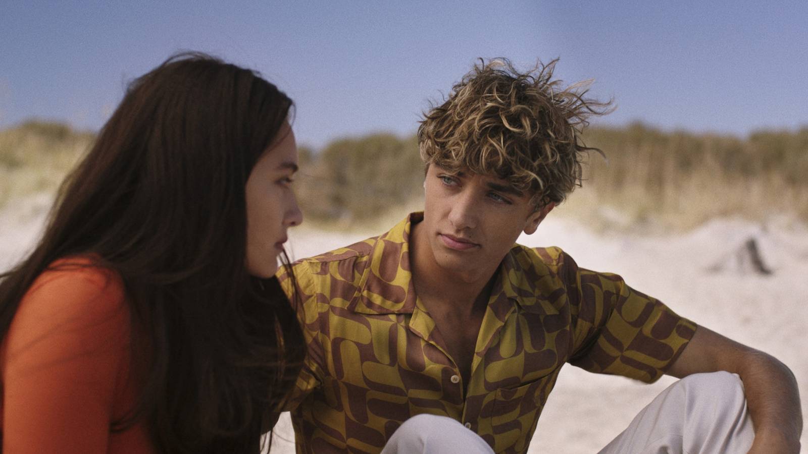 Belly (Lola Tung) and Conrad (Gavin Casalegno) looking at each other on the beach in The Summer I Turned Pretty