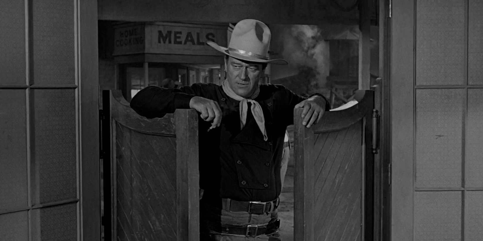 John Wayne leans against saloon doors while smoking in The Man Who SH๏τ Liberty Valance