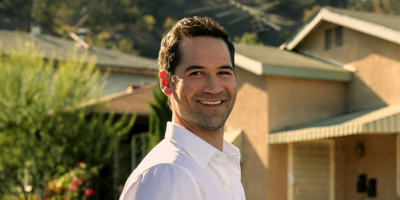 Mickey Haller, played by Manuel Garcia-Rulfo, smiles while standing in front of his house in The Lincoln Lawyer.