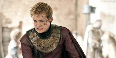 Joffrey Baratheon covered in dirt and a cut on his cheek, as a fight breaks out behind him, in Game of Thrones.