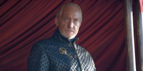 Charles Dance as Tywin Lannister staring off at something as he stands in front of a red curtain in Game of Thrones.