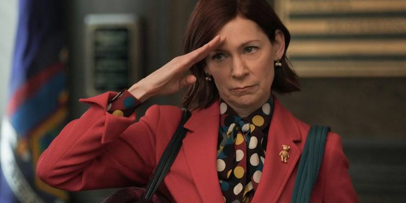 Elsbeth in a red suit, saluting with a stern face