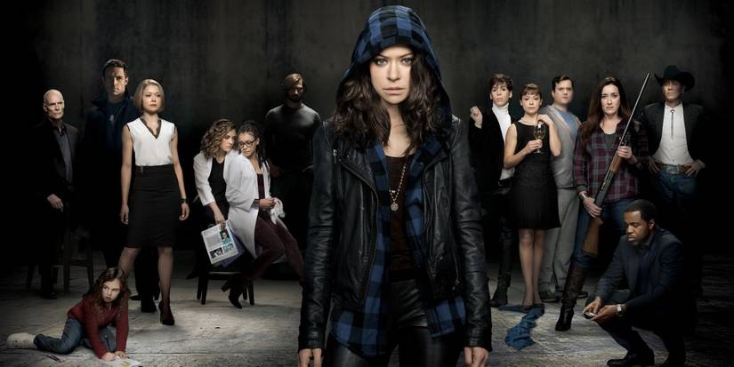 Tatiana Maslany usando um moletom e em pé em frente aos personagens principais de Orphan Black