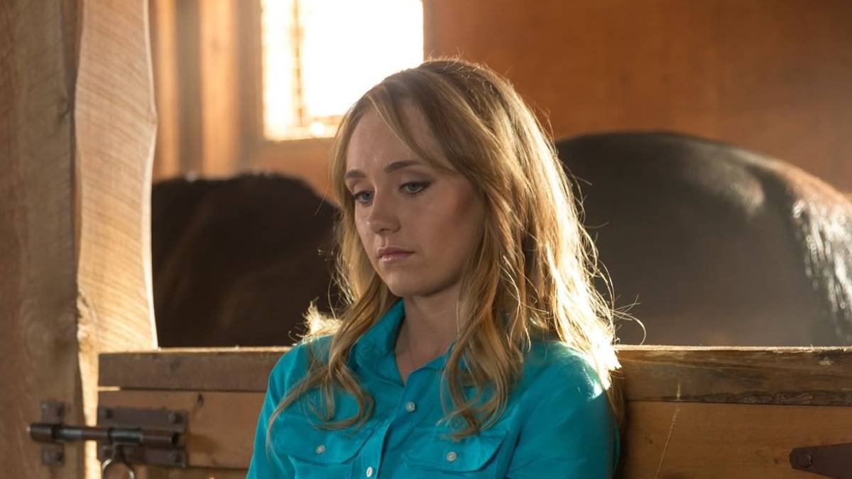 Amy in a blue shirt, looking sad in a stable