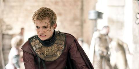 Joffrey Baratheon, covered in dirt and with a cut on his cheek, as a fight breaks out behind him, in Game of Thrones.