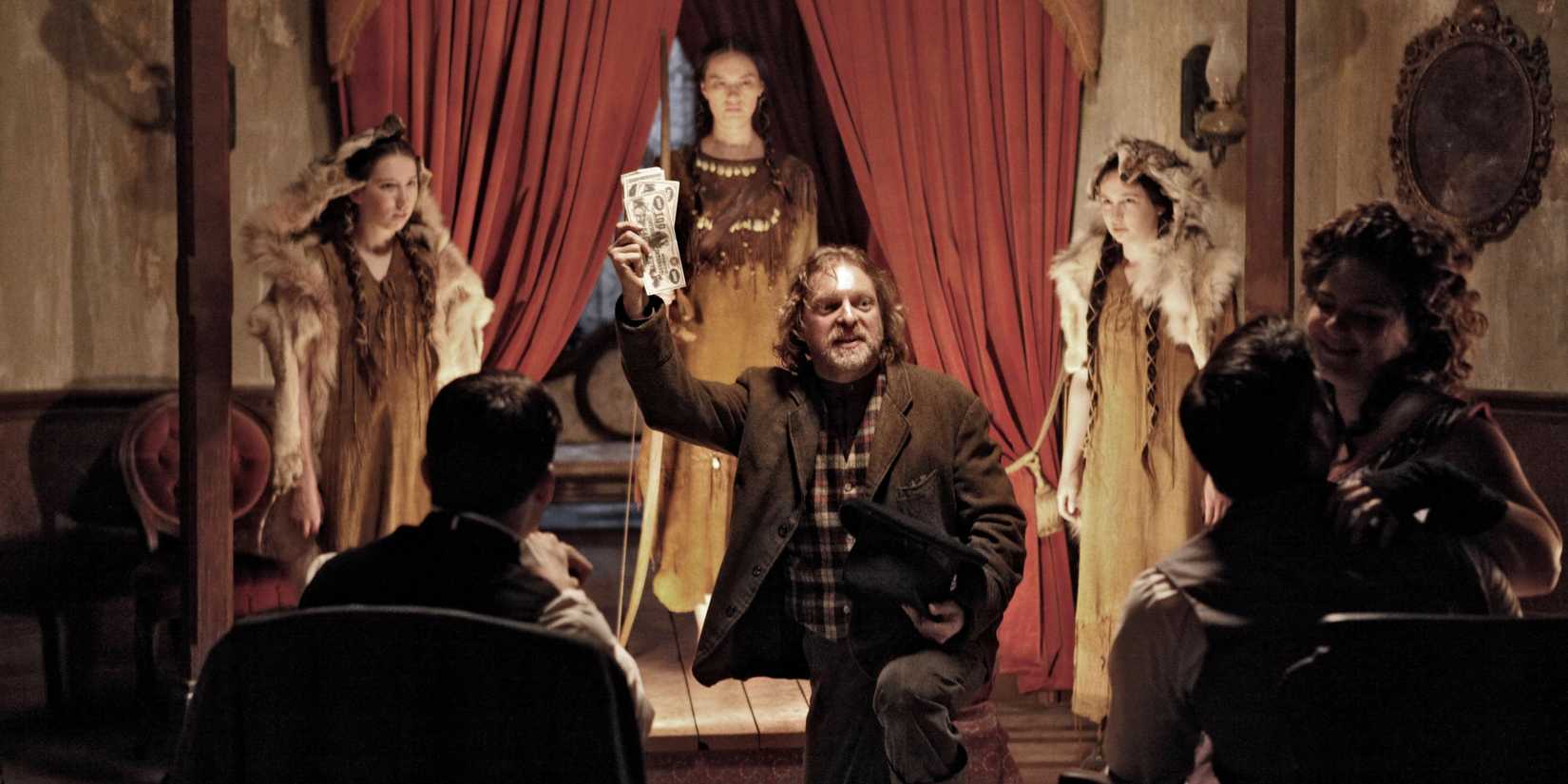 A group shot of Michelle Creber, Cara Gee, and Matreya Scarrwener in an old Western room. It looks like the women are being auctioned off to men. Show Strange Empire
