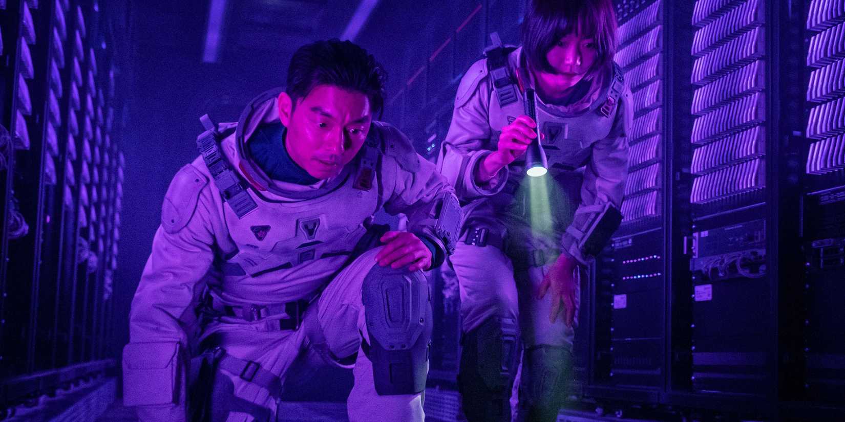 Bae Doona e Gong Yoo mirando uma lanterna para baixo para algo abaixo do piso da nave espacial no Mar Silent