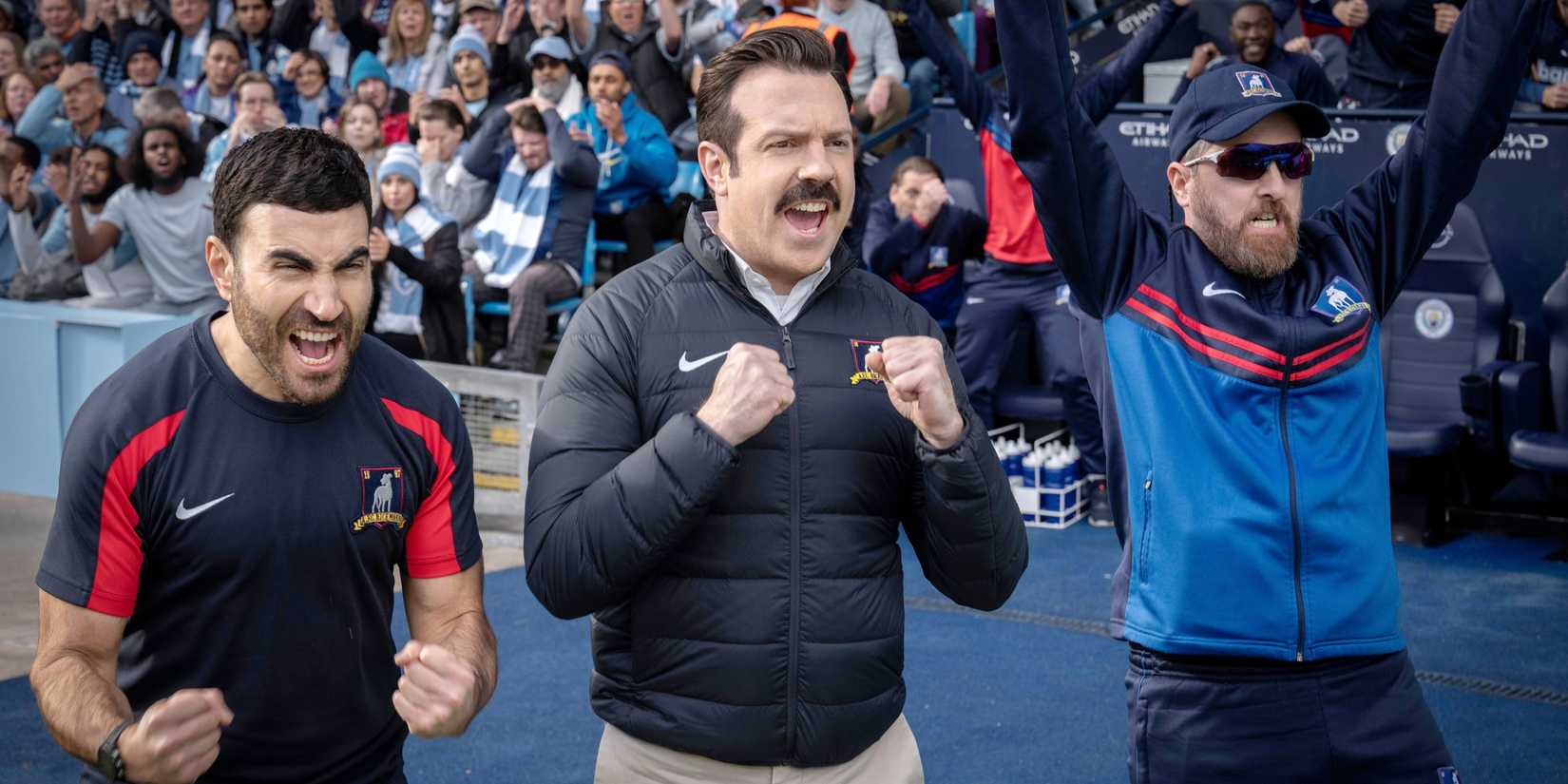 Brett Goldstein, Jason Sudeikis and Brendan Hunt cheer from the sidelines in a scene from Ted Lasso