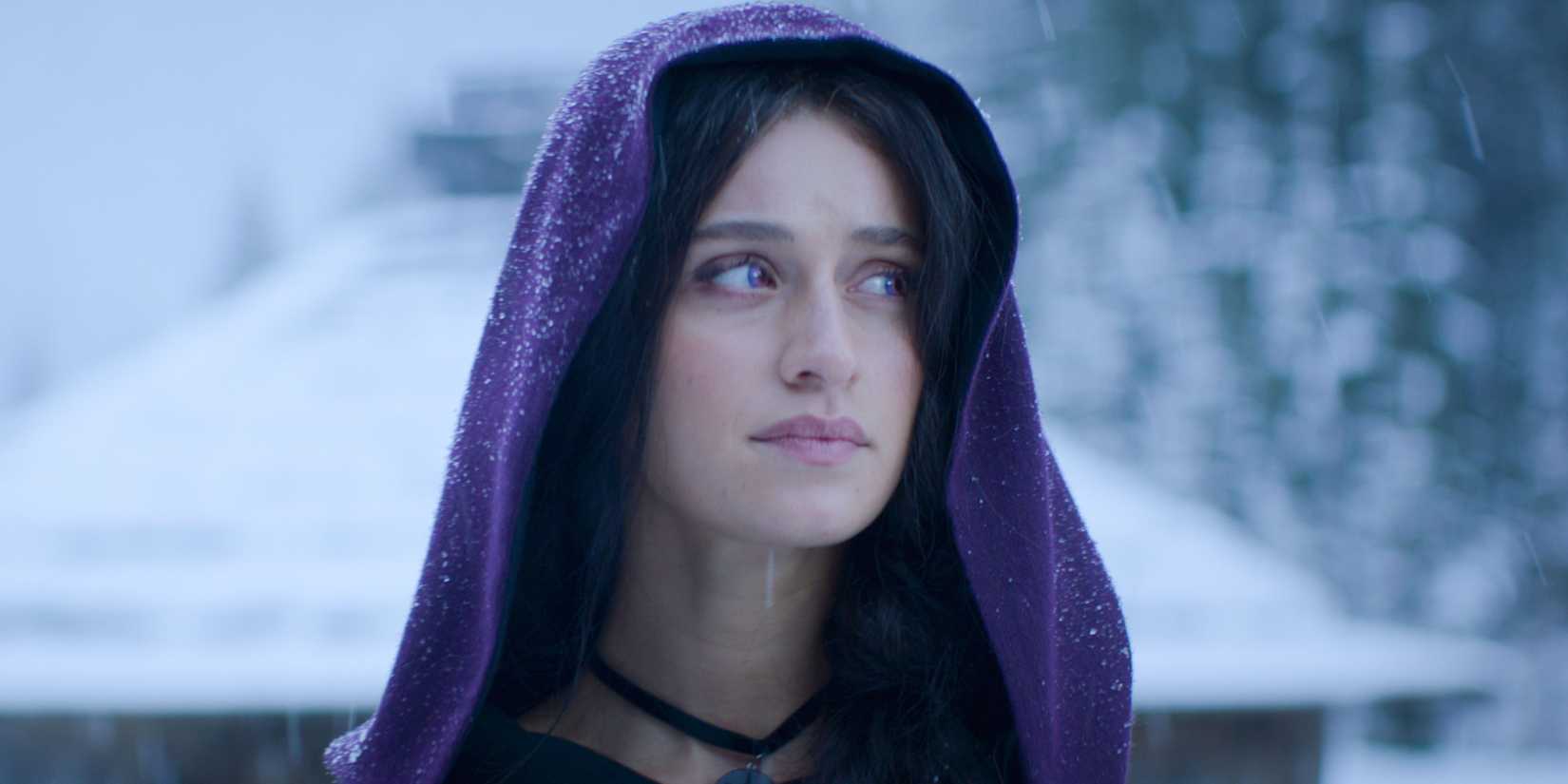 Close-up of Anya Chalotra as Yennefer of Vengerberg peering to the right, dressed in a purple-hooded robe in The Witcher