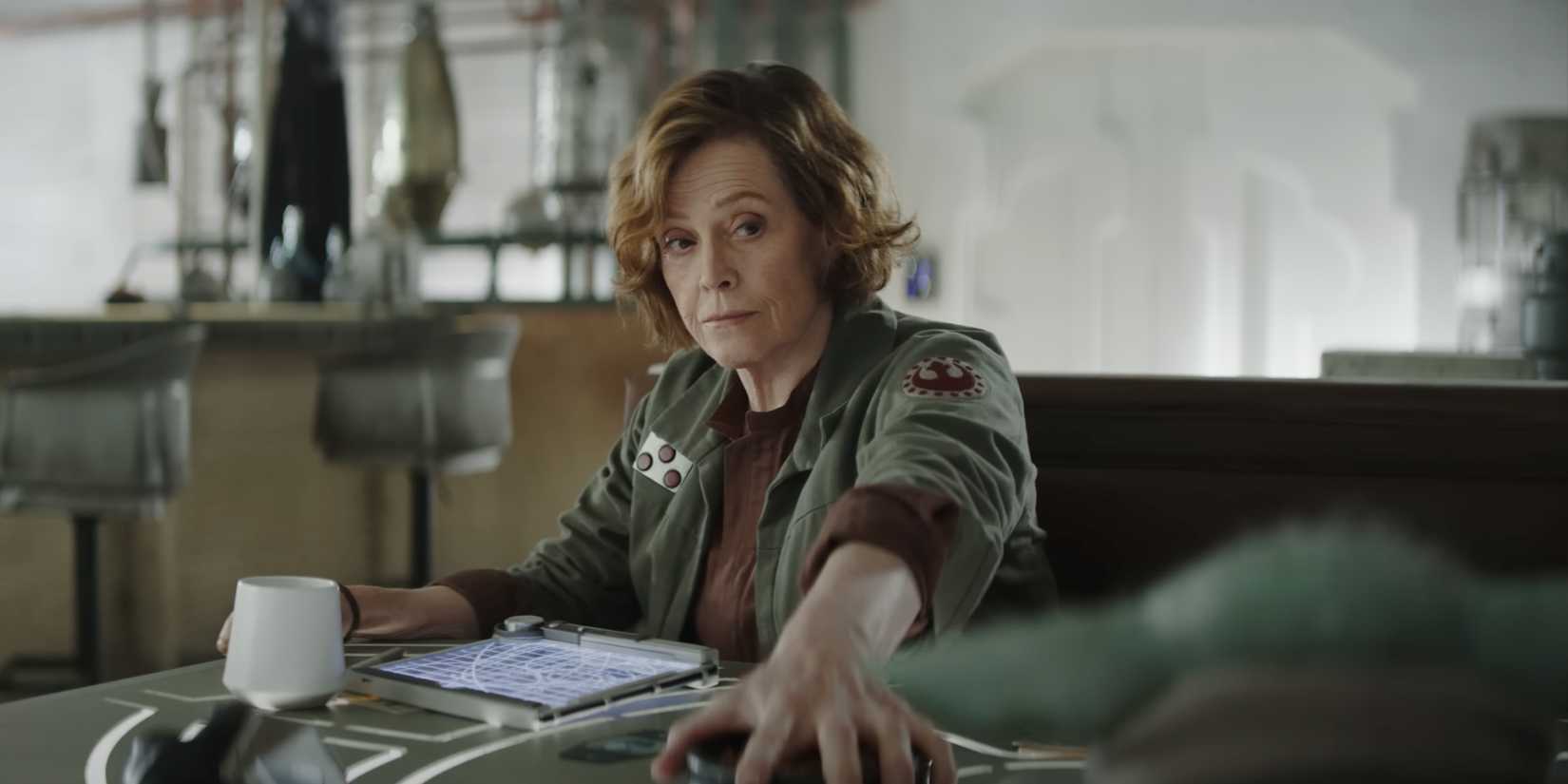 Colonel Ward (Sigourney Weaver) holds a bowl of snacks away from Grogu and levels him with a look.