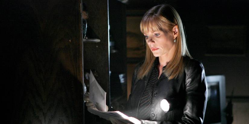 Catherine (Marg Helgenberger) with her flashlight out in a dark room as she examines papers in CSI