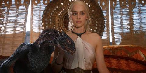 Emilia Clarke as Daenerys Targaryen sitting with a small Drogon next to her in Game of Thrones