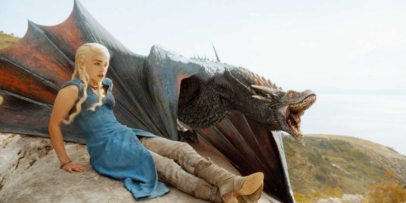 Daenerys Targaryen (Emilia Clarke) sitting on a rock beside her dragon in Game of Thrones