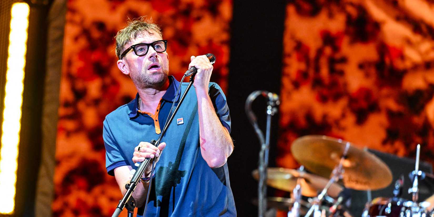 Damon Albarn in blue shirt holding microphone