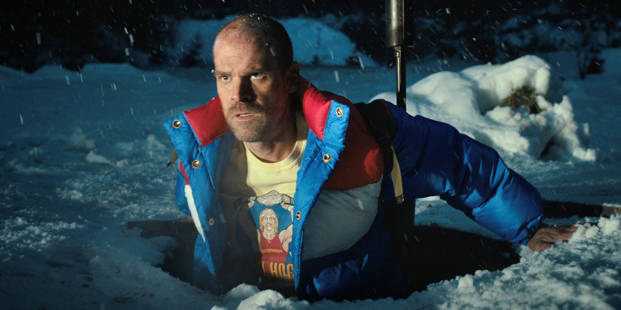 David Harbour's Hopper looking worried while coming out of a hole in the snow in Stranger Things season 4