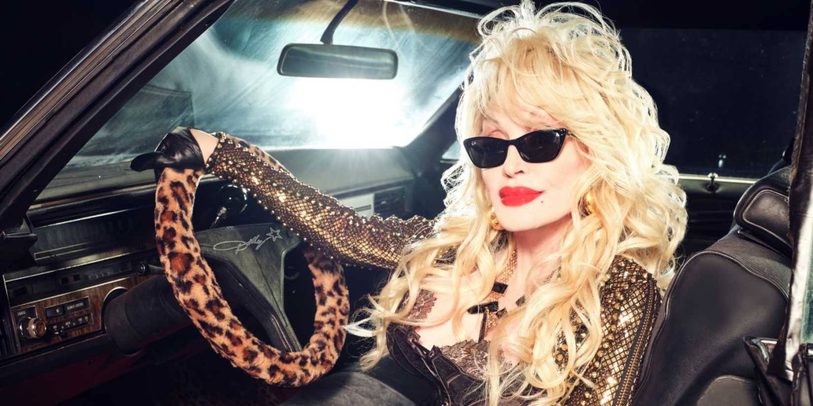 Dolly Parton sitting in a convertible car, wearing sunglasses and a studded leather jacket.