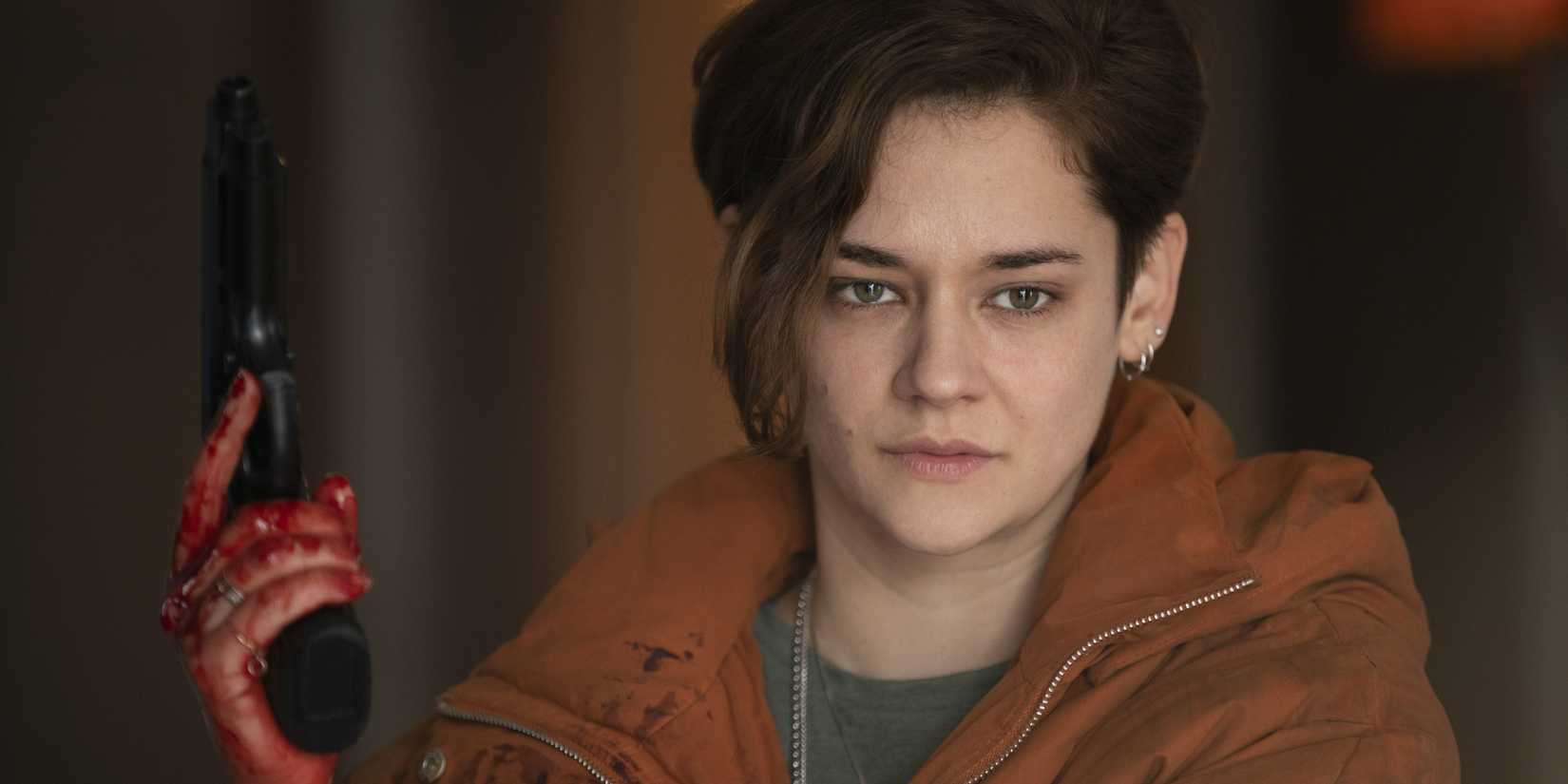 Emma with a bloodied hand holding a gun in Marianne